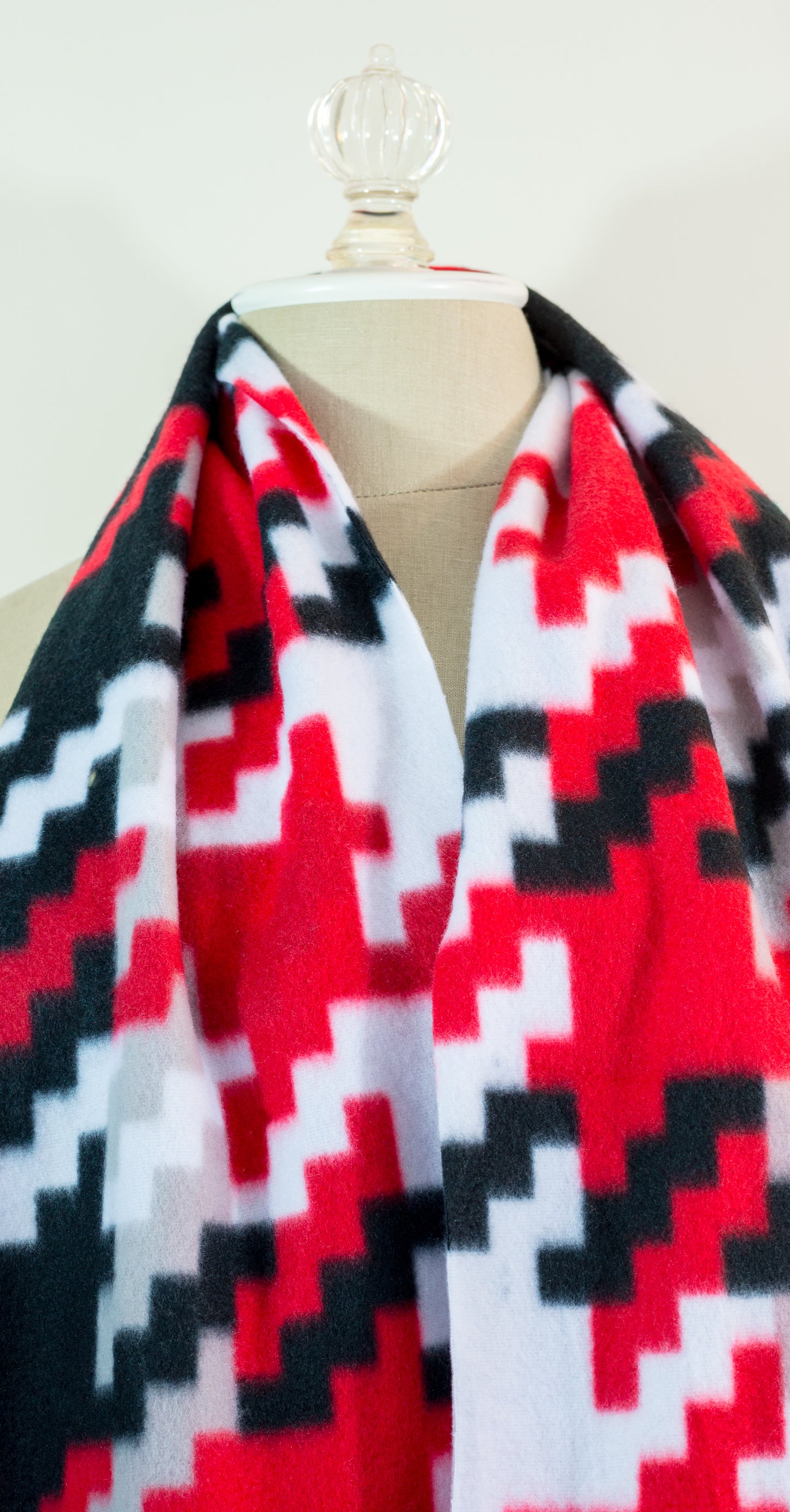 A scarf with a geometric houndstooth pattern in red, black, white, and beige colors, displayed on a flat surface.
Photo by Karen King [additional_image_link]