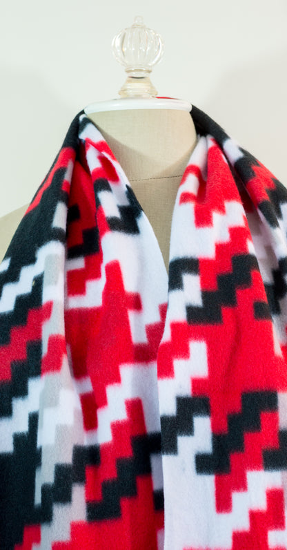 A scarf with a geometric houndstooth pattern in red, black, white, and beige colors, displayed on a flat surface.
Photo by Karen King [additional_image_link]