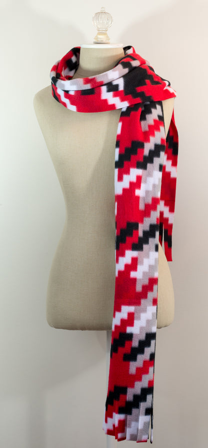 A scarf with a geometric houndstooth pattern in red, black, white, and beige colors, displayed on a flat surface.
Photo by Karen King [additional_image_link]