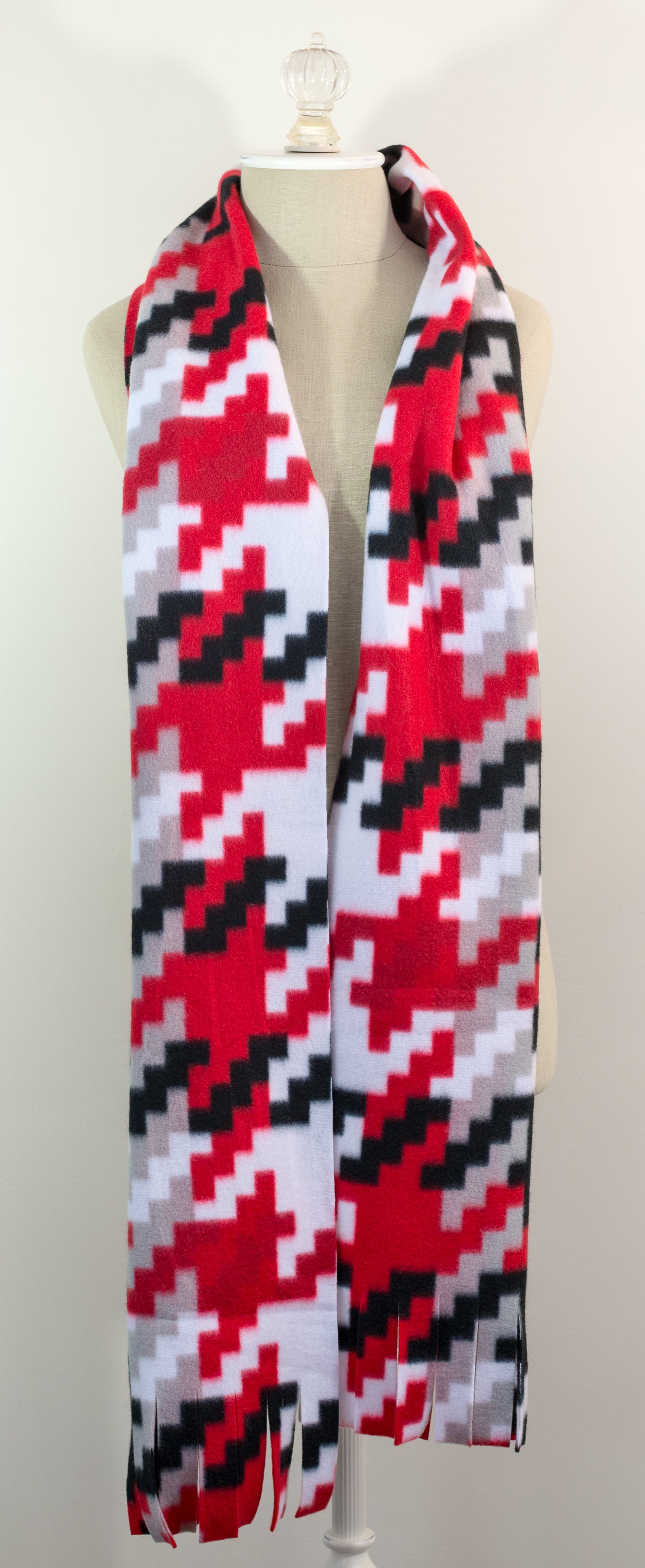 A scarf with a geometric houndstooth pattern in red, black, white, and beige colors, displayed on a flat surface.
Photo by Karen King [additional_image_link]