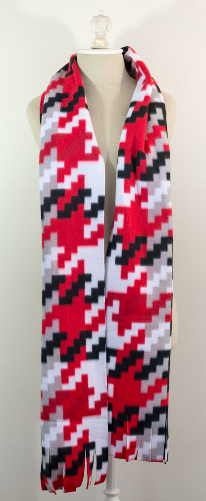 A scarf with a geometric houndstooth pattern in red, black, white, and beige colors, displayed on a flat surface.
Photo by Karen King [additional_image_link]