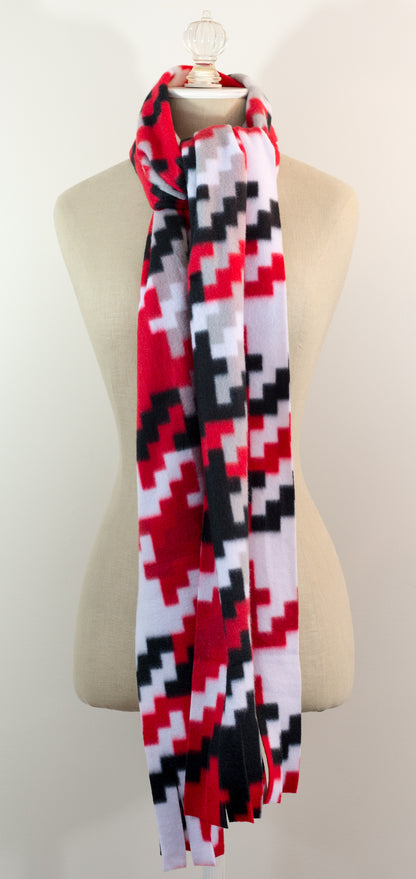 A scarf with a geometric houndstooth pattern in red, black, white, and beige colors, displayed on a flat surface.
Photo by Karen King [additional_image_link]