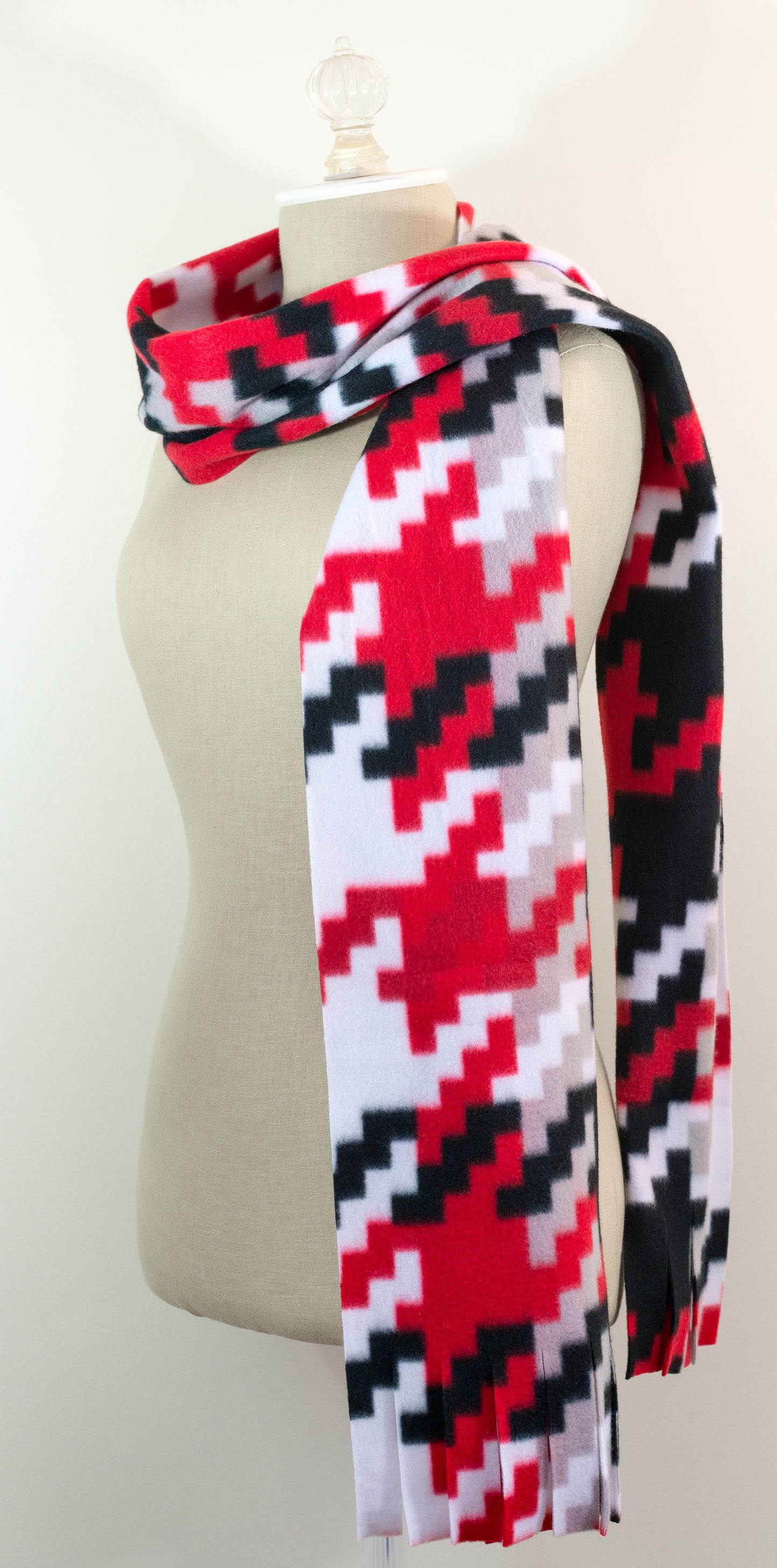 A scarf with a geometric houndstooth pattern in red, black, white, and beige colors, displayed on a flat surface.
Photo by Karen King [additional_image_link]