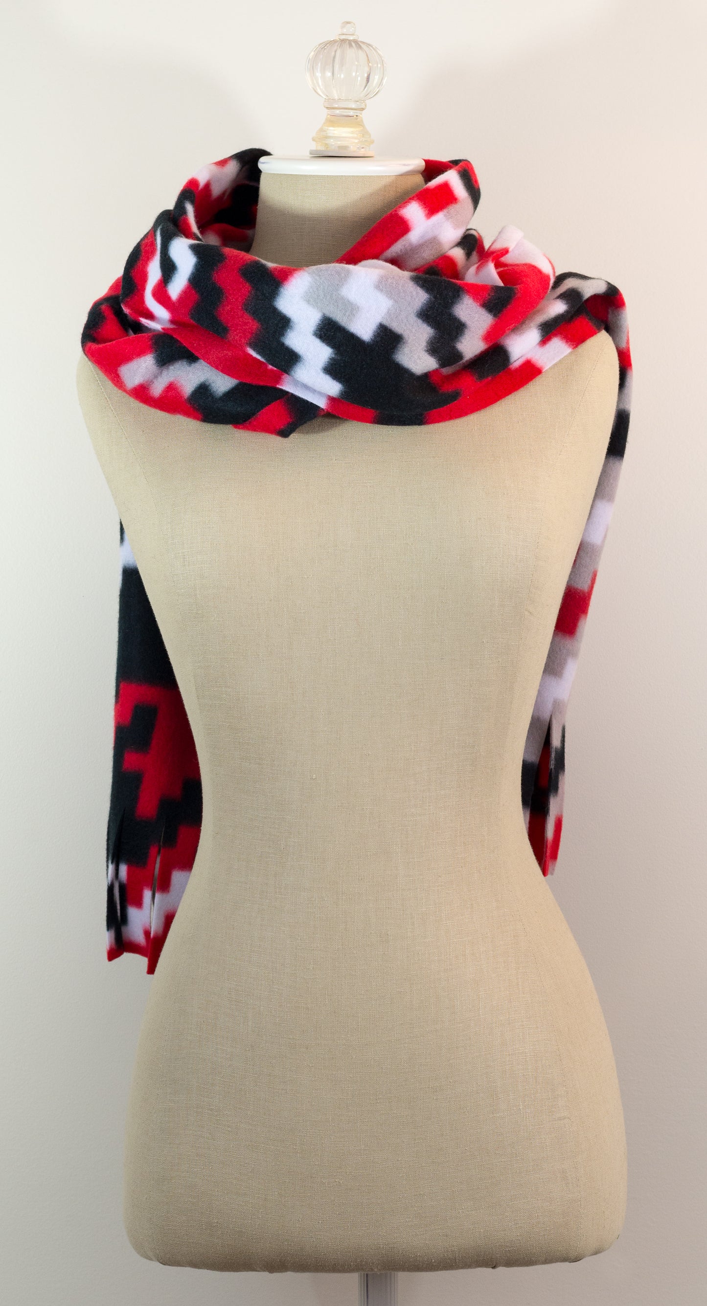 A scarf with a geometric houndstooth pattern in red, black, white, and beige colors, displayed on a flat surface.
Photo by Karen King [additional_image_link]