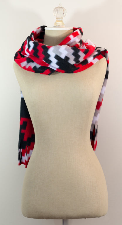A scarf with a geometric houndstooth pattern in red, black, white, and beige colors, displayed on a flat surface.
Photo by Karen King [additional_image_link]