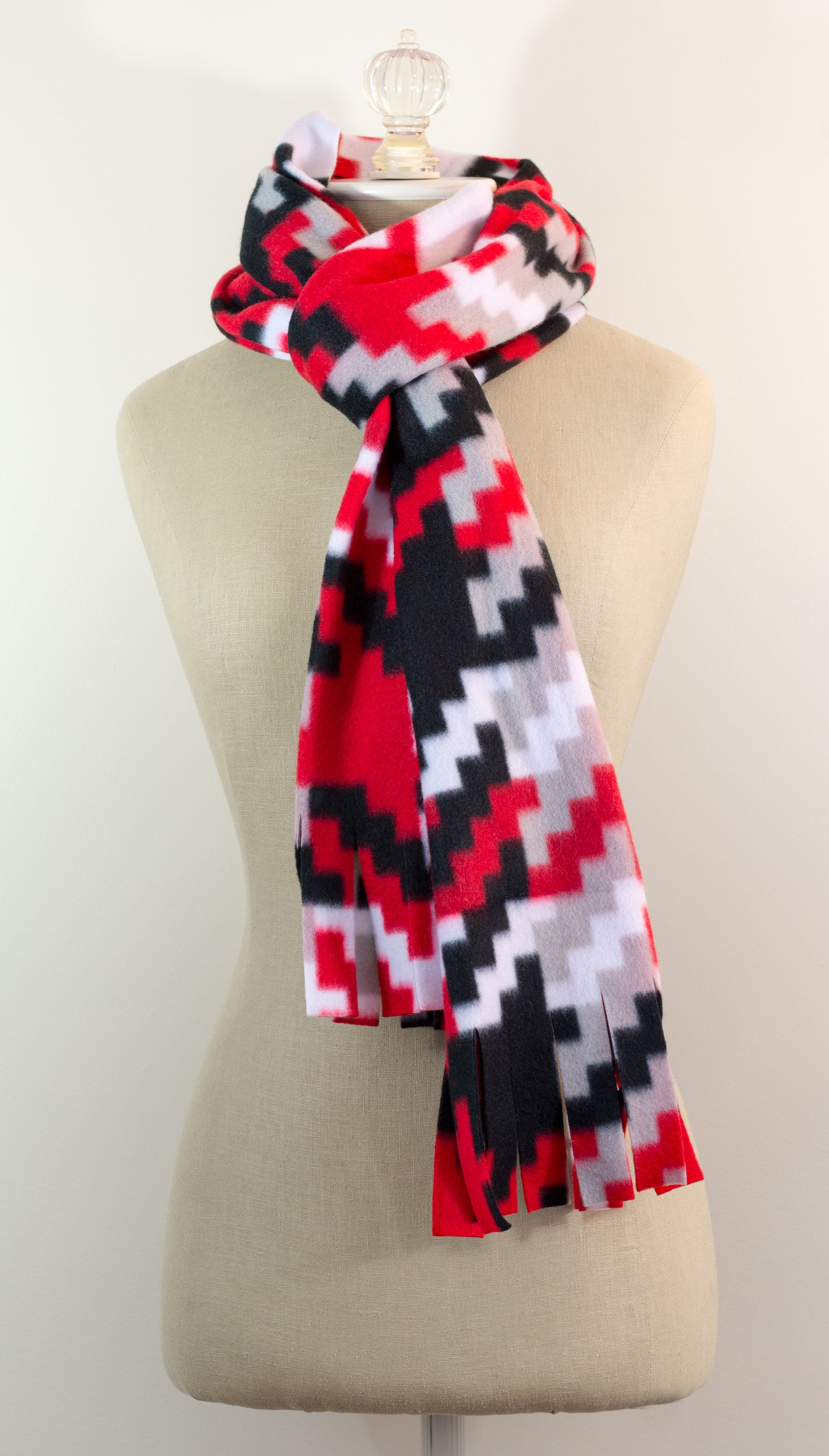 A scarf with a geometric houndstooth pattern in red, black, white, and beige colors, displayed on a flat surface.
Photo by Karen King [additional_image_link]