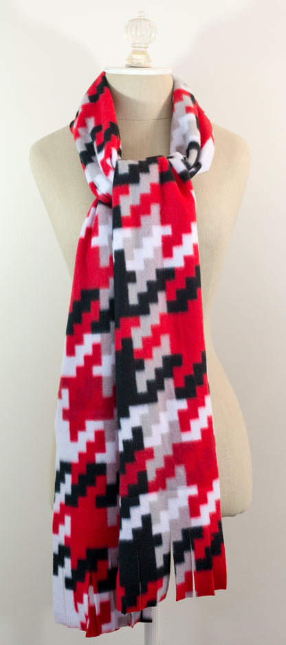 A scarf with a geometric houndstooth pattern in red, black, white, and beige colors, displayed on a flat surface.
Photo by Karen King [additional_image_link]