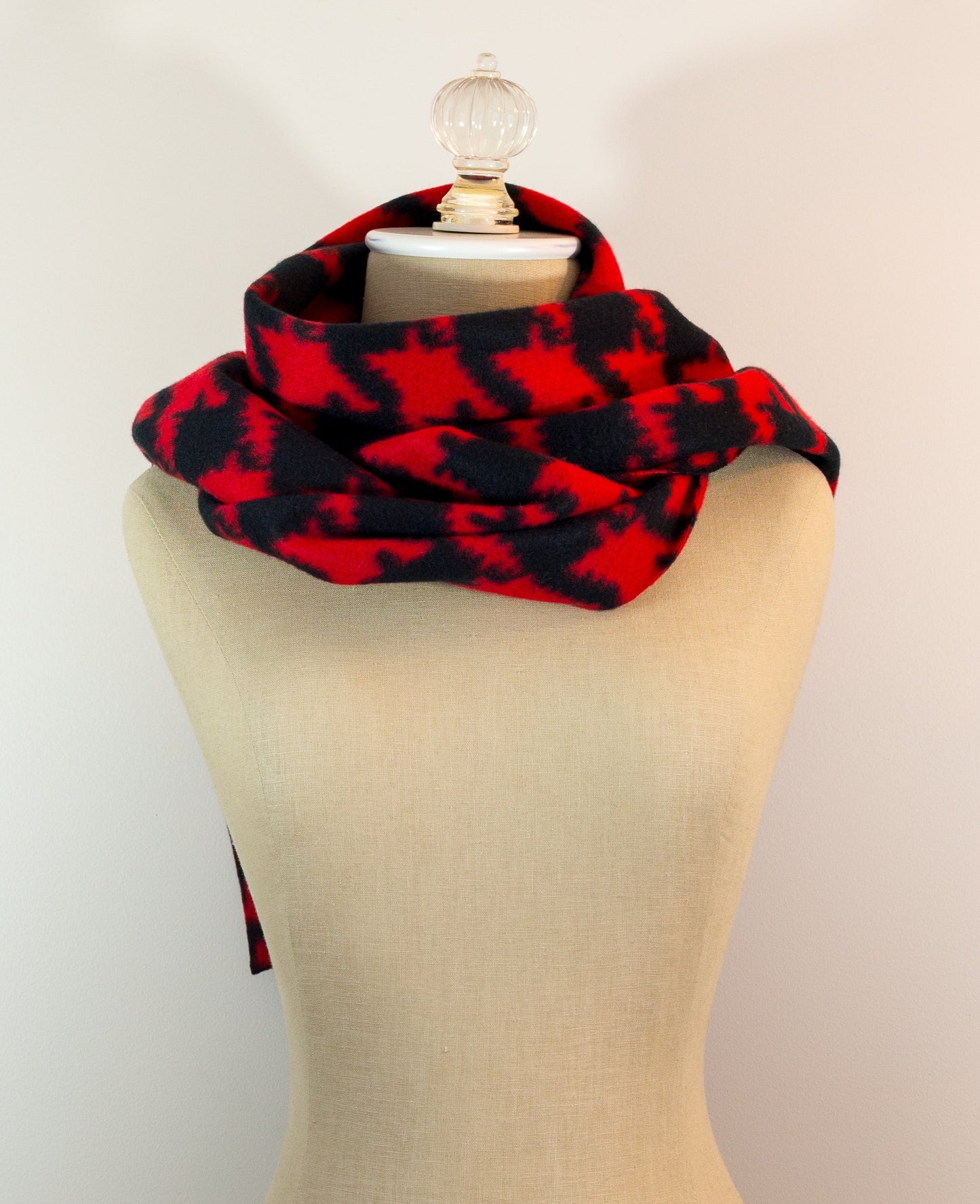 A scarf with a geometric houndstooth pattern in shades of red and black, displayed on a mannequin.
Photo by Karen King [additional_image_link]
