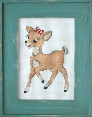 A framed cross-stitch artwork featuring a brown deer with white markings and a red bow on a white fabric background, surrounded by a distressed teal wooden frame.
Photo by Tiny Modernist [additional_image_link]