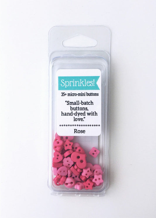 Packaging of rose pink sprinkle buttons, with some buttons visible through the clear plastic, labeled with the brand name and product details.
Photo by JustAnotherButtonCompany.com [image_link]