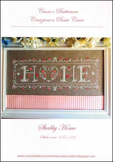 A cross stitch kit depicting the word 'Home' with floral embellishments, presented in a display box with a pink and white striped background, containing linen, floss, and embroidery scissors.
Photo by CuoreBatticuore.com [additional_image_link]