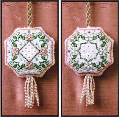 Two views of a handmade octagonal cross-stitch ornament with a tassel, featuring pink flowers, green leaves, and a central diamond motif on a white fabric background, set against a brown textured backdrop.
Photo by The Sweetheart Tree [image_link]