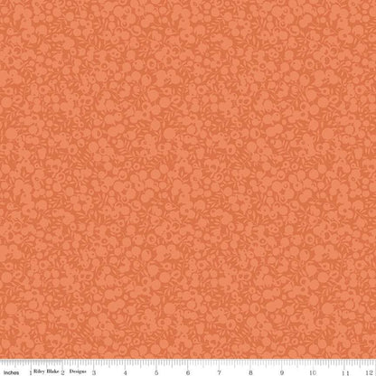 A close-up of a fabric or wallpaper pattern in warm orange and peach tones, with a repeating small floral or vine motif. A ruler strip is visible along the bottom edge showing scale.
Photo by RileyBlakeDesigns.com [additional_image_link]