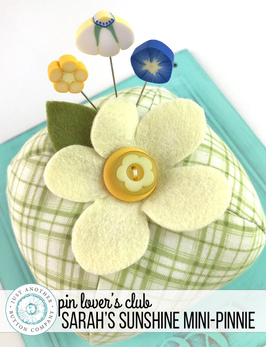 A handmade pincushion kit featuring a floral pattern with yellow wool felt, green wool felt, and a green square print background. Includes the text 'Just Another Button Company' and 'Pin Lover's Club'.
Photo by JustAnotherButtonCompany.com [image_link]