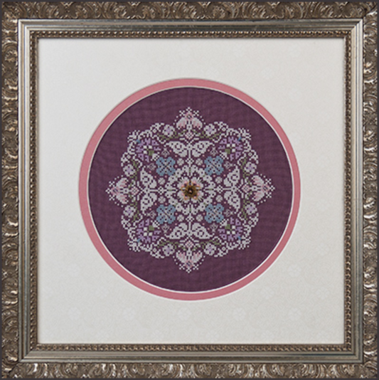A framed cross stitch embroidery kit depicting a snowflake pattern with purple, blue, and green colors, encased in a decorative frame.
Photo by JustNan.com [image_link]