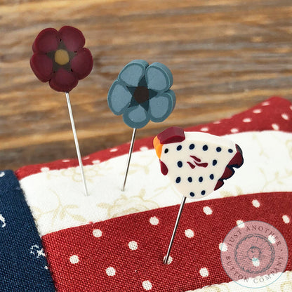 A 'Star Spangled' mini pincushion by Just Another Button Company featuring a red, white, and blue color scheme with a star pattern, placed on a wooden surface with a 'Pin Lover's Club' label and branding.
Pins included.
Photo by JustAnotherButtonCompany.com [additional_image_link]