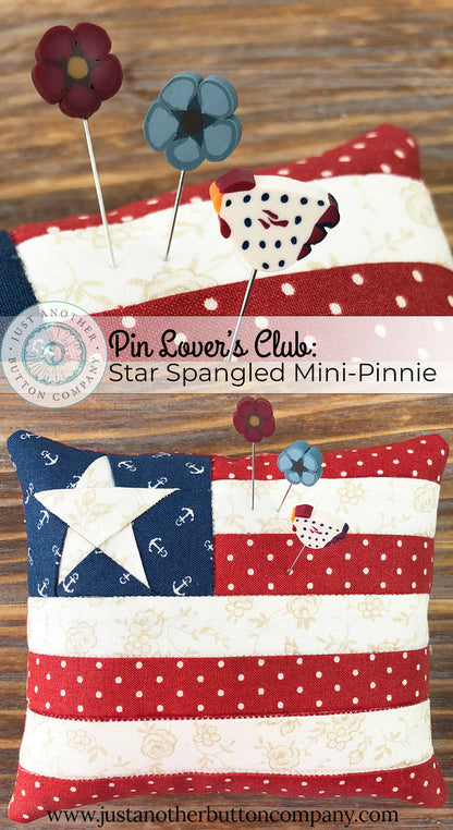 A 'Star Spangled' mini pincushion by Just Another Button Company featuring a red, white, and blue color scheme with a star pattern, placed on a wooden surface with a 'Pin Lover's Club' label and branding.
Photo by JustAnotherButtonCompany.com [additional_image_link]