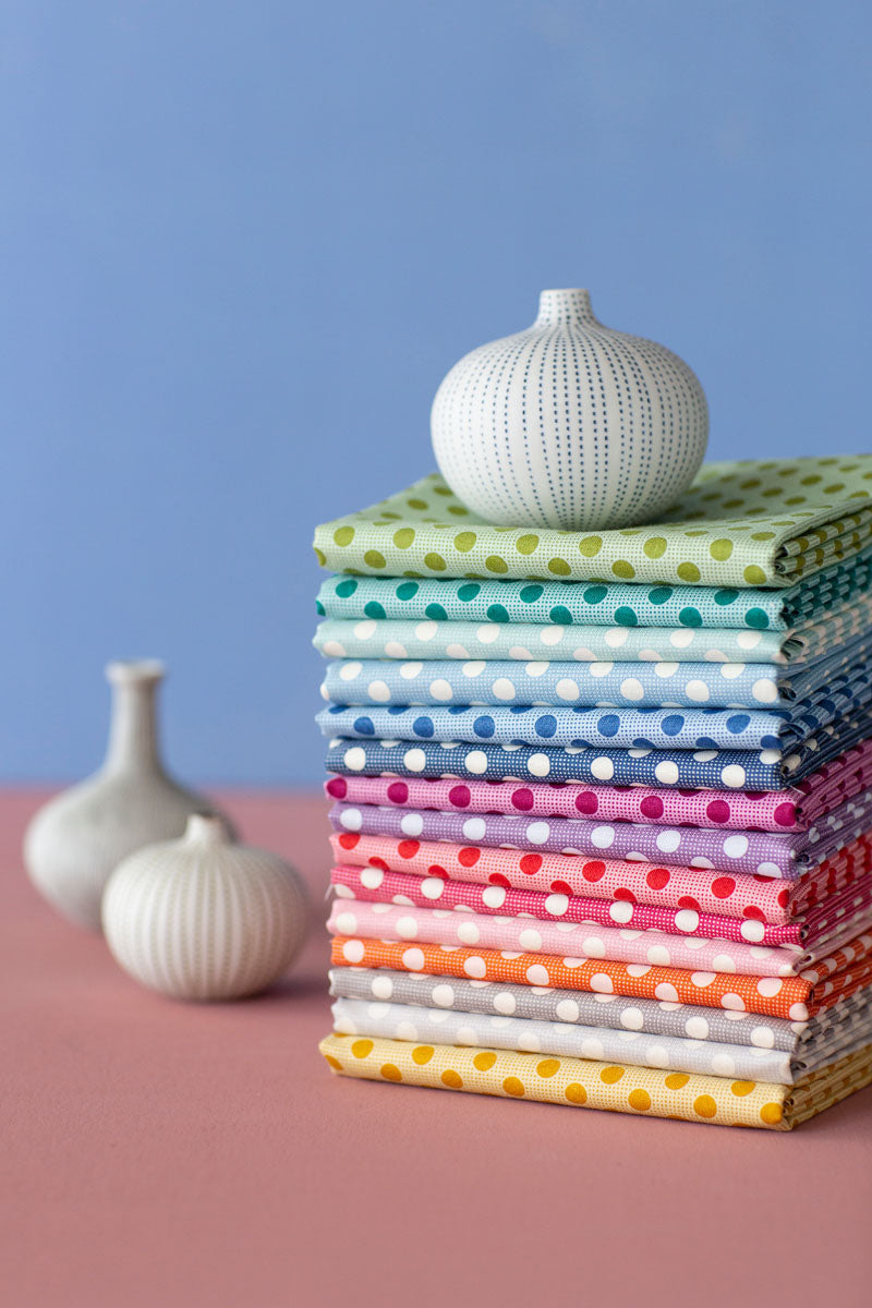 Stack of colorful polka dot fabric on a pink surface with white vases against a blue background.
Photo by Tildafabrics.com [additional_image_link]