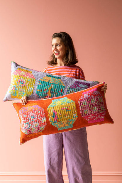 A woman holding two colorful, quilted rectangular throw pillows against a solid peach-pink background.
Photo by Tildafabrics.com [image_link]
