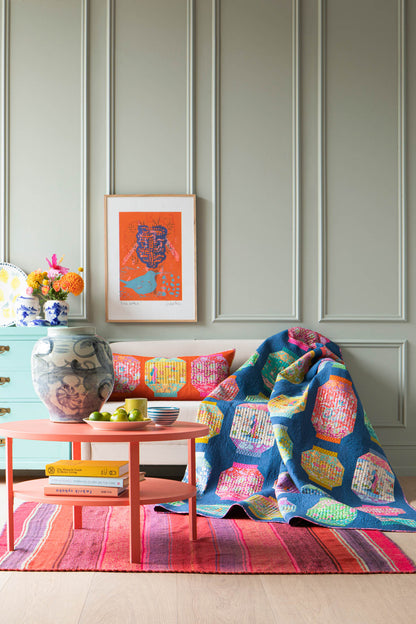 A colorful patchwork quilt draped over a bench in a styled room with paneled walls, a pink coffee table, and a striped rug.
Photo by Tildafabrics.com [additional_image_link]