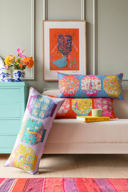 Three colorful patchwork lumbar throw pillows displayed on a light pink bench in a styled room setting with a mint green cabinet, framed art, and a striped rug.
Photo by Tildafabrics.com [additional_image_link]
