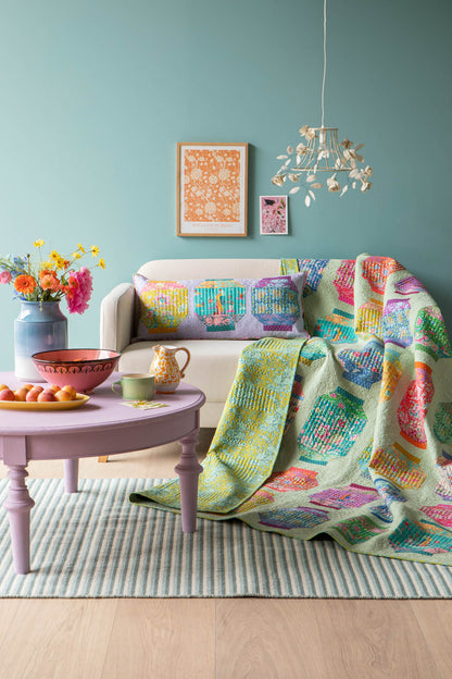 A colorful patchwork quilt draped over a white sofa in a styled living room with a pastel blue wall, lavender coffee table, and striped rug.
Photo by Tildafabrics.com [additional_image_link]