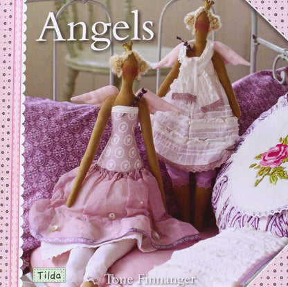 A book cover titled "Angels" by Tone Finnanger, featuring two fabric angel dolls in pink and white dresses posed on a bed with purple bedding.
Photo by Tildafabrics.com [additional_image_link]