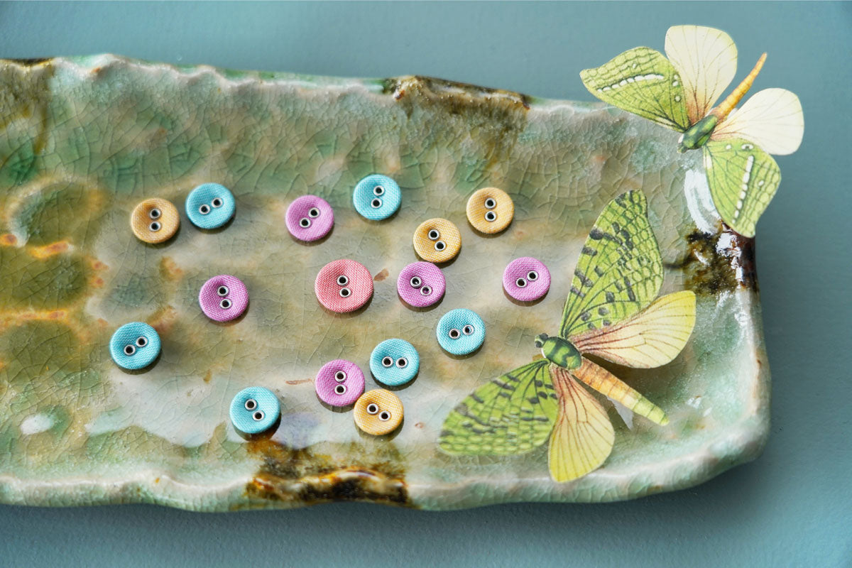 Decorative ceramic dish with colorful buttons and butterfly designs on a blue background.
Photo by Tildafabrics.com [additional_image_link]