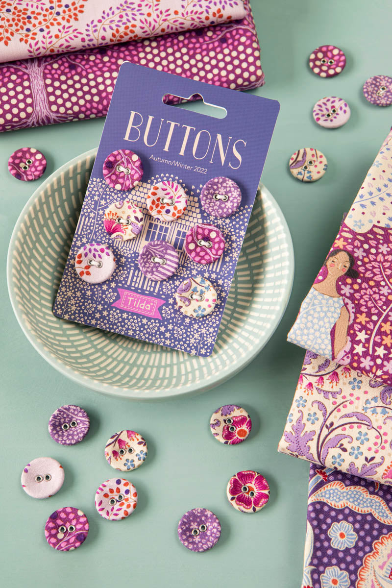 A package of buttons labeled 'BUTTONS' and 'Tilda' sits on a patterned plate, surrounded by matching fabric pieces and loose buttons in a styled flat-lay arrangement.
Photo by Tildafabrics.com [additional_image_link]
