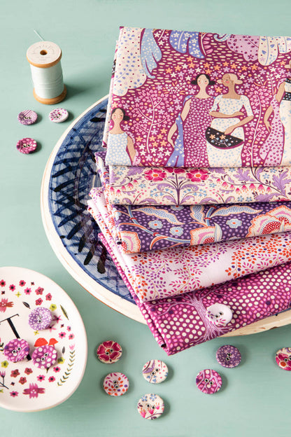 A stack of folded patterned fabric pieces in pink, purple, and white tones, arranged on a blue-and-white plate with decorative buttons, thread, and a small dish on a mint green background.
Photo by Tildafabrics.com [additional_image_link]