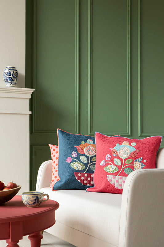 Three decorative quilted throw pillows on a white sofa in a styled living room setting with a green paneled wall, a red side table, and a white fireplace mantel.
Photo by Tildafabrics.com [image_link]