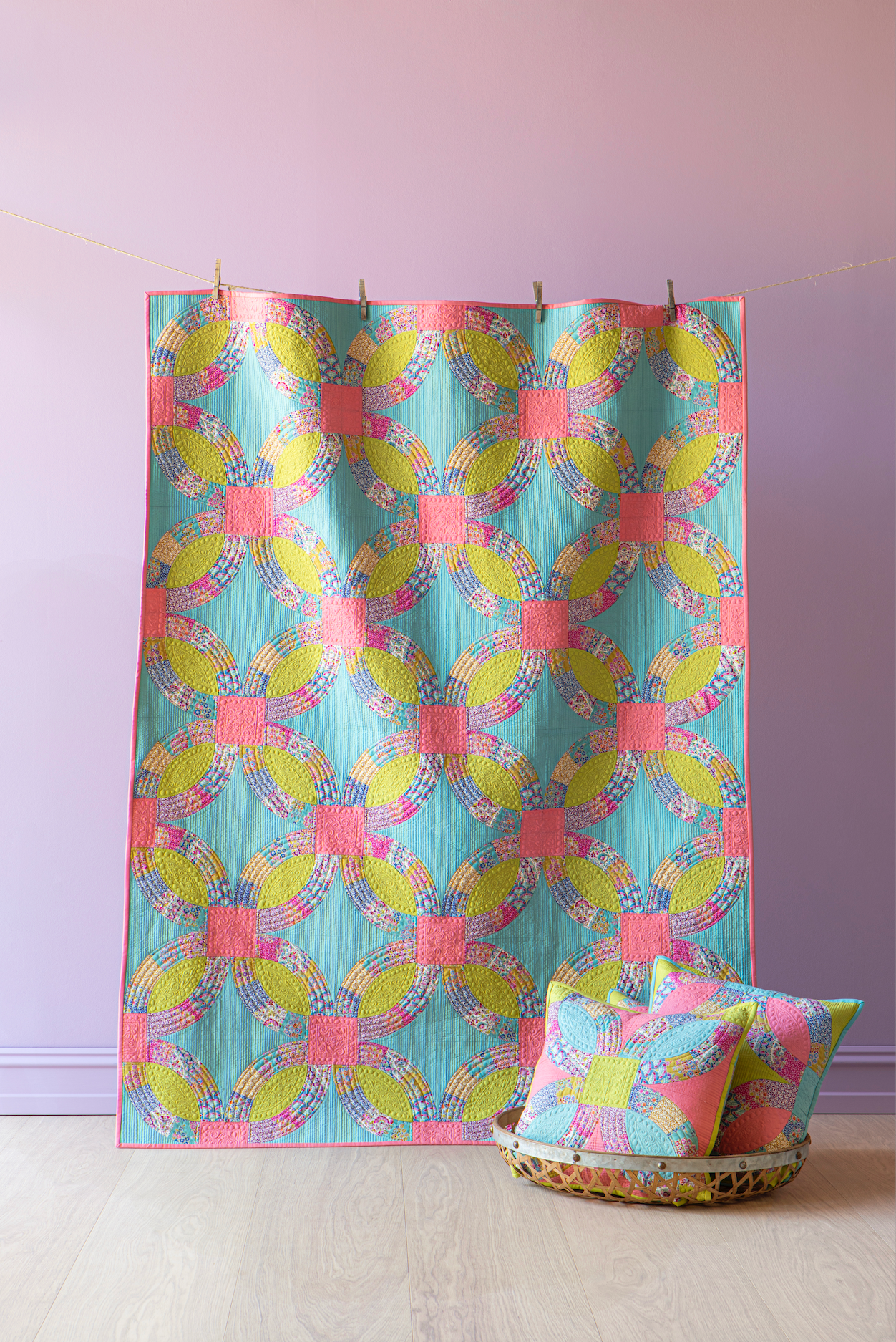 A colorful patterned quilt with matching throw pillows, hanging against a lavender wall on a light wood floor.
Photo by Tildafabrics.com [additional_image_link]
