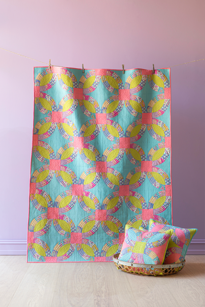 A colorful patterned quilt with matching throw pillows, hanging against a lavender wall on a light wood floor.
Photo by Tildafabrics.com [additional_image_link]