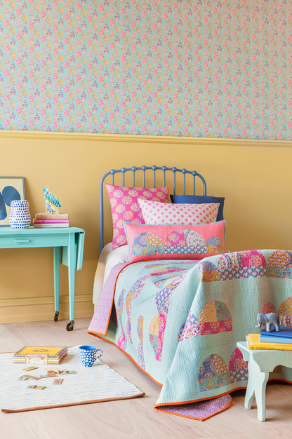 A colorful children's bedroom featuring a light blue quilted patchwork bedspread with elephant motifs, pink patterned pillows, a blue metal bed frame, a yellow wainscoted wall, and a mint green side table.
Photo by Tildafabrics.com [additional_image_link]