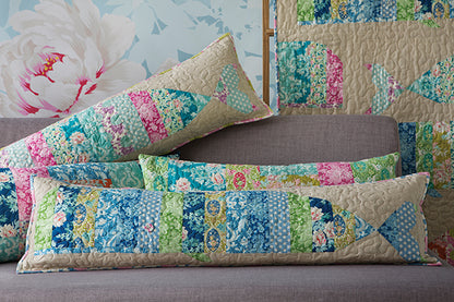 A set of patchwork fish-shaped lumbar pillows in shades of blue, green, pink, and beige, styled on a gray sofa with a matching patchwork quilt in the background.
Photo by Tildafabrics.com [additional_image_link]