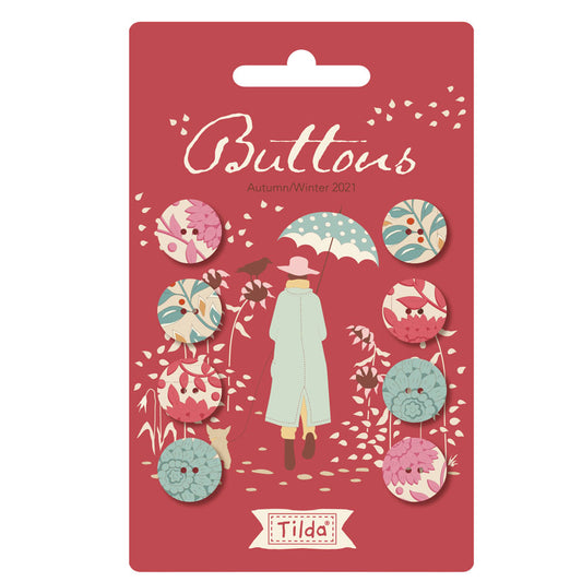 Tilda Buttons Autumn/Winter 2021 carded pack featuring 8 decorative buttons with floral and bird patterns in pink, teal, and cream, displayed on a red backing card with a whimsical illustration.
Photo by Tildafabrics.com [image_link]