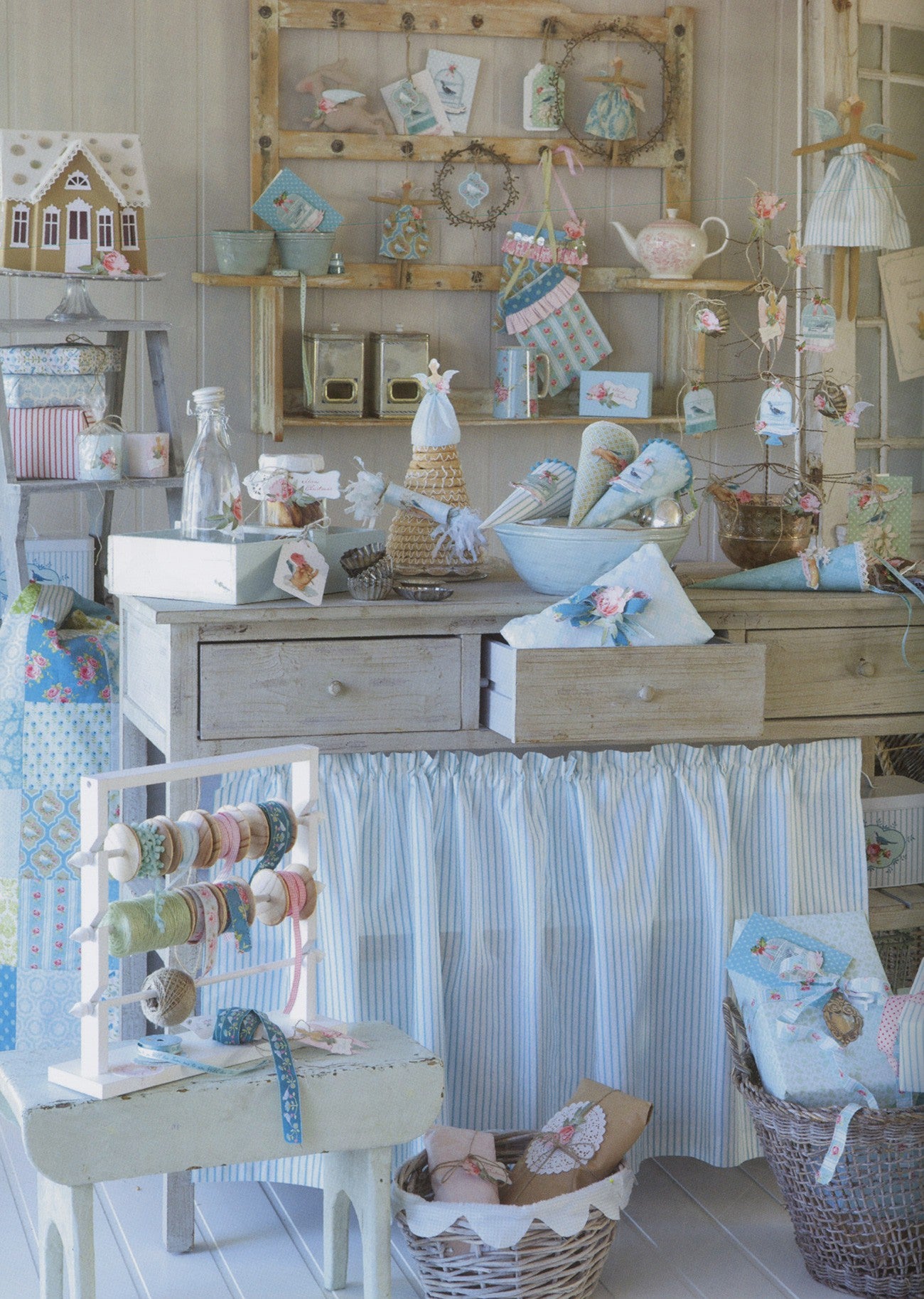 A styled vintage-inspired craft or sewing room display featuring a light wood desk with a blue and white striped fabric skirt, surrounded by sewing supplies, yarn spools, baskets, and small decorative items.
Photo by Tildafabrics.com [additional_image_link]
