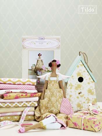 Woman in a gold dress standing next to a birdhouse and fabric stack with Tilda branding.
Photo by Tildafabrics.com [additional_image_link]
