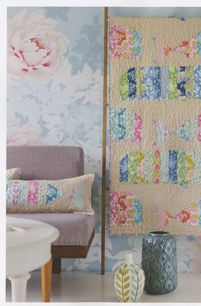A colorful photo featuring patterned quilts and pillows styled on a wooden stool against a floral wallpaper background.
Photo by Tildafabrics.com [additional_image_link]