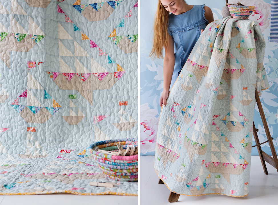 A quilted throw blanket with a patchwork design of light blue, beige, and multicolor floral/bunting motifs, shown both as a close-up detail and being held up by a woman in a blue dress.
Photo by Tildafabrics.com [additional_image_link]