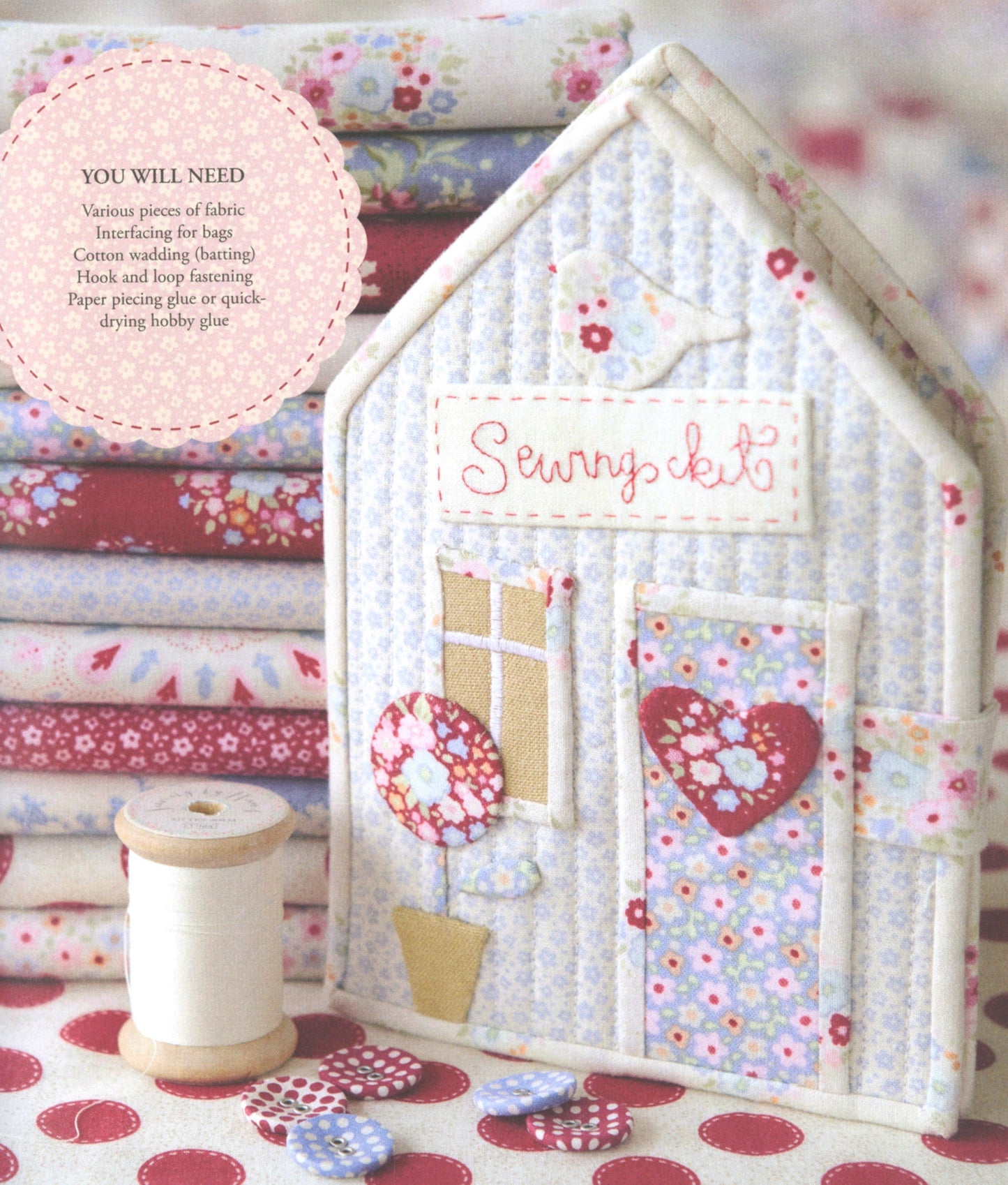 A handmade quilted house-shaped sewing kit display made from floral and paisley fabrics, with a spool of thread and folded fabric stacks in the background. A circular text callout lists included materials.
Photo by Tildafabrics.com [additional_image_link]