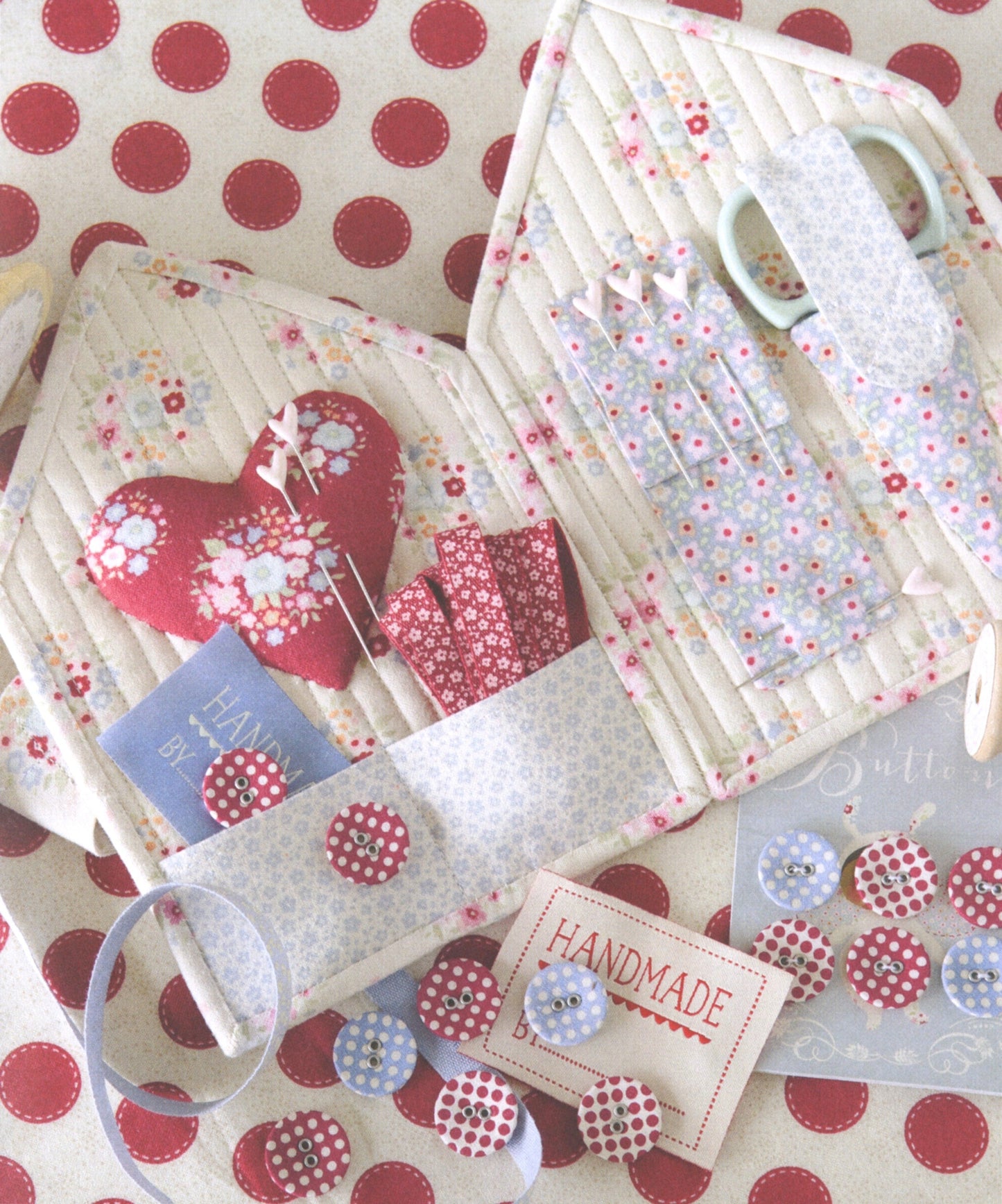 A handmade fabric organizer set with quilted pouches, floral patterned fabric, buttons, ribbon, and scissors arranged on a red and cream polka dot surface.
Photo by Tildafabrics.com [additional_image_link]