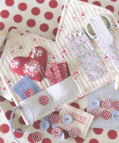 A handmade fabric organizer set with quilted pouches, floral patterned fabric, buttons, ribbon, and scissors arranged on a red and cream polka dot surface.
Photo by Tildafabrics.com [additional_image_link]