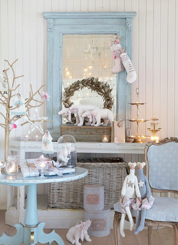 A styled holiday interior scene with a large distressed light blue mirror, a blue side table, wicker baskets, candles, a wreath, plush toys, and stockings against white paneled walls.
Photo by Tildafabrics.com [additional_image_link]