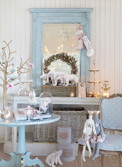 A styled holiday interior scene with a large distressed light blue mirror, a blue side table, wicker baskets, candles, a wreath, plush toys, and stockings against white paneled walls.
Photo by Tildafabrics.com [additional_image_link]