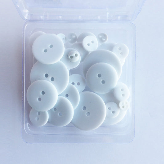 A clear plastic container holding 25 white, matte finish buttons in varying sizes, designed for crafting and sewing projects.
Photo by JustAnotherButtonCompany.com [image_link]