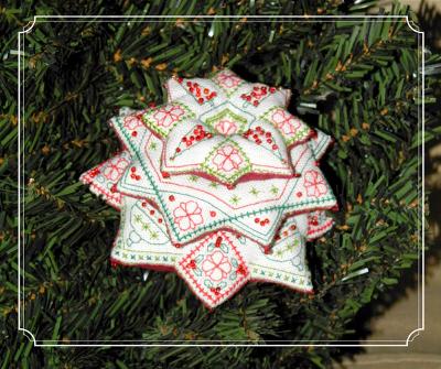 A handmade embroidered star ornament in white fabric with red and green floral patterns, displayed on a green pine tree branch.
[image_link]